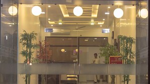 La entrada del Hotel Kamran Palace con fachada de vidrio, señalización iluminada y plantas en macetas.