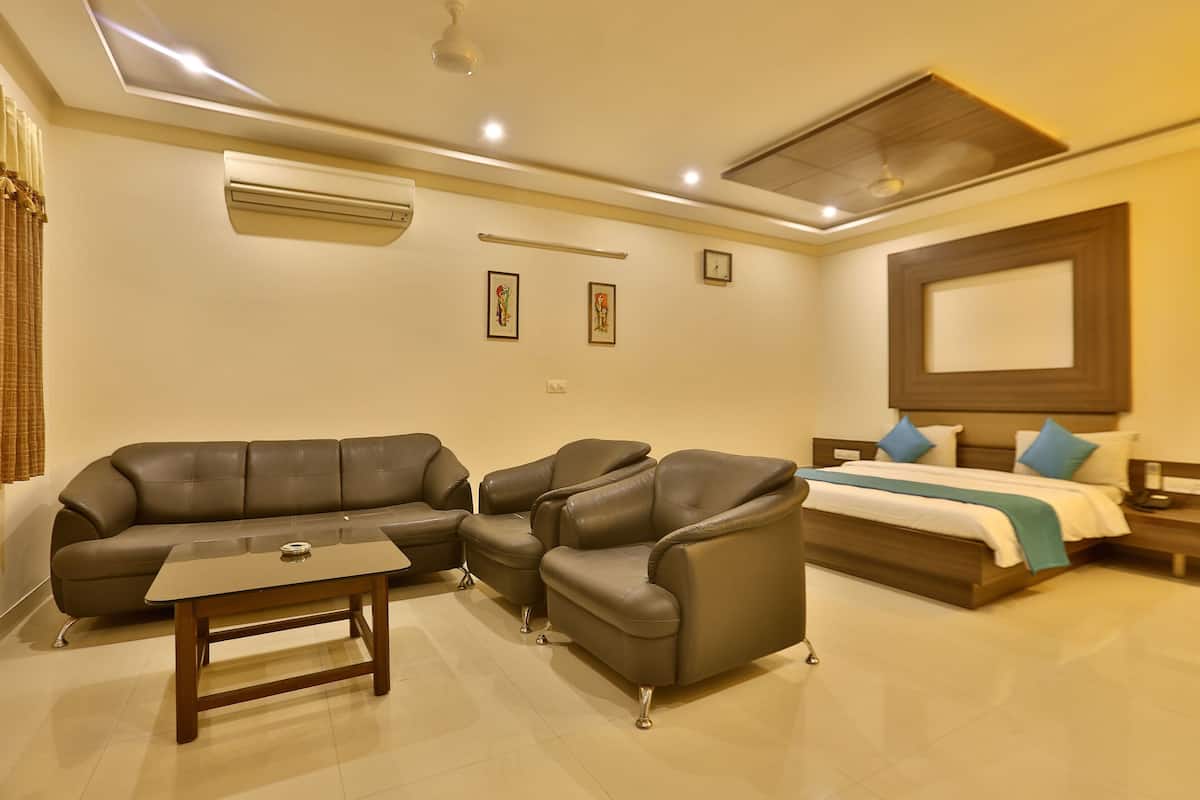A modern hotel room with a sofa, armchair, and a bed with a wooden headboard.