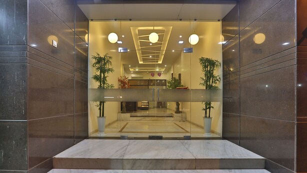 Un vestíbulo de hotel moderno con escalones de mármol que conducen a la recepción, puertas de cristal y plantas en macetas.