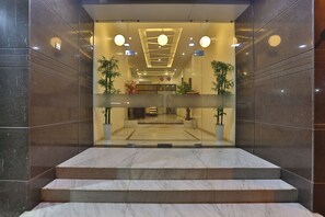 Un vestíbulo de hotel moderno con escalones de mármol que conducen a la recepción, puertas de cristal y plantas en macetas.