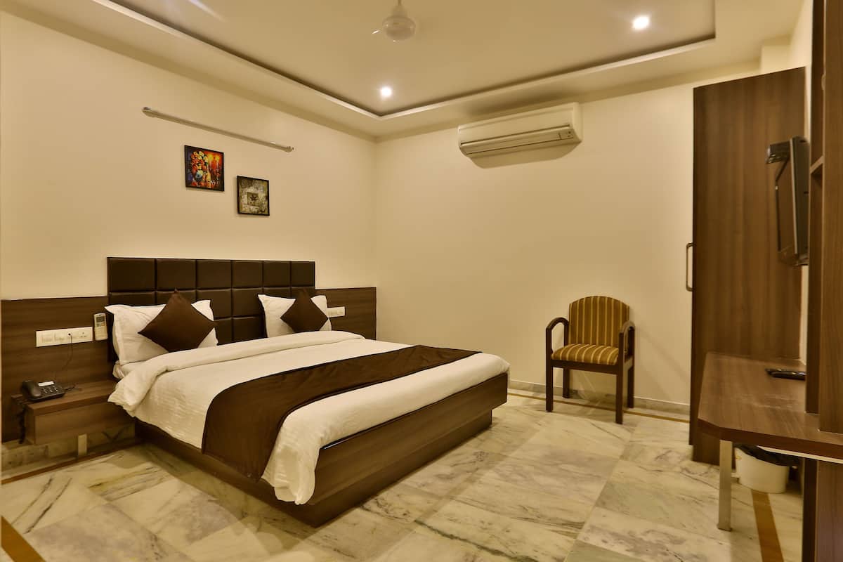 A hotel room with a large bed, a bedside table with a phone, a chair, a wardrobe, and an air conditioning unit.