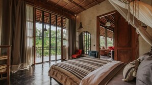 Une chambre spacieuse avec un grand lit, un plafond en bois et de grandes fenêtres donnant sur un paysage verdoyant.