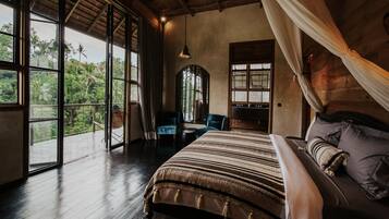A spacious bedroom with a large bed, a window with curtains, a small table, and a chair.
