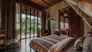 A spacious bedroom with a large bed, wooden flooring, and a view of lush greenery through large windows. - Exceptional 9BR Incredible Jungle View, River Access (Ubud)
