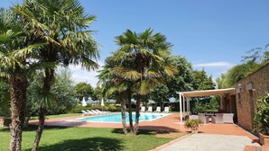 A pool area with palm trees, a covered patio, and a stone building. - Timeless Tuscan Holiday Stay (Unknown)