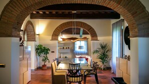 A dining area with a glass table, chairs, and a brick archway overhead. - Timeless Tuscan Holiday Stay (Unknown)