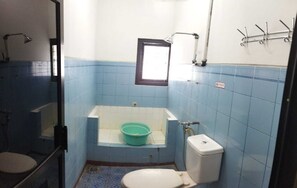 A small bathroom with blue tiles, a toilet, a bathtub with a green basin, and a window. - Baciro Homestay46 (Yogyakarta)