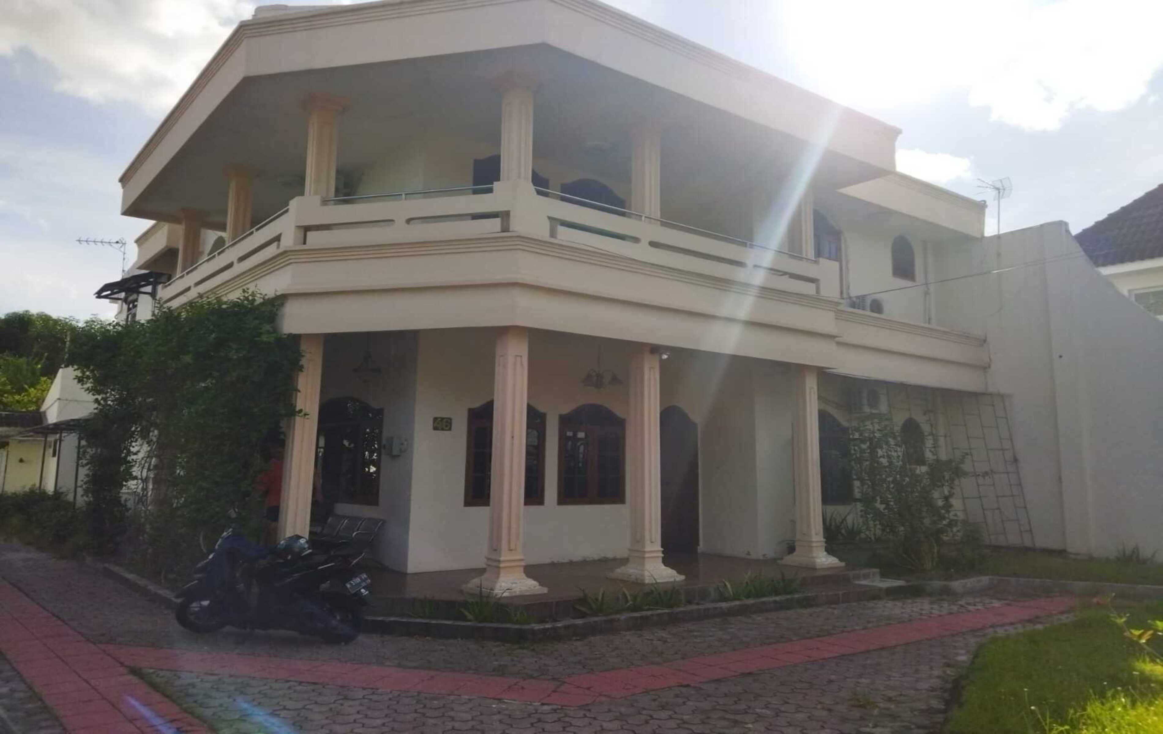 A two-story building with a balcony, columns, and a paved entrance.