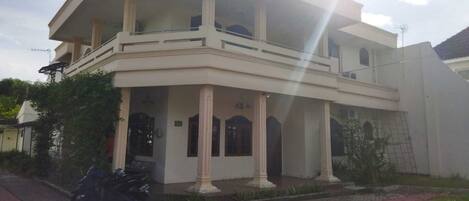 A two-story building with a balcony, columns, and a paved entrance.