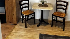 Une pièce comprenant une armoire en bois, deux chaises en bois foncé avec des assises en osier, une petite table ronde ornée d’un pot de fleurs et un grand tableau accroché au mur.