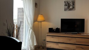 Un salon avec un téléviseur posé sur un meuble en bois, une lampe et une fenêtre avec des rideaux.