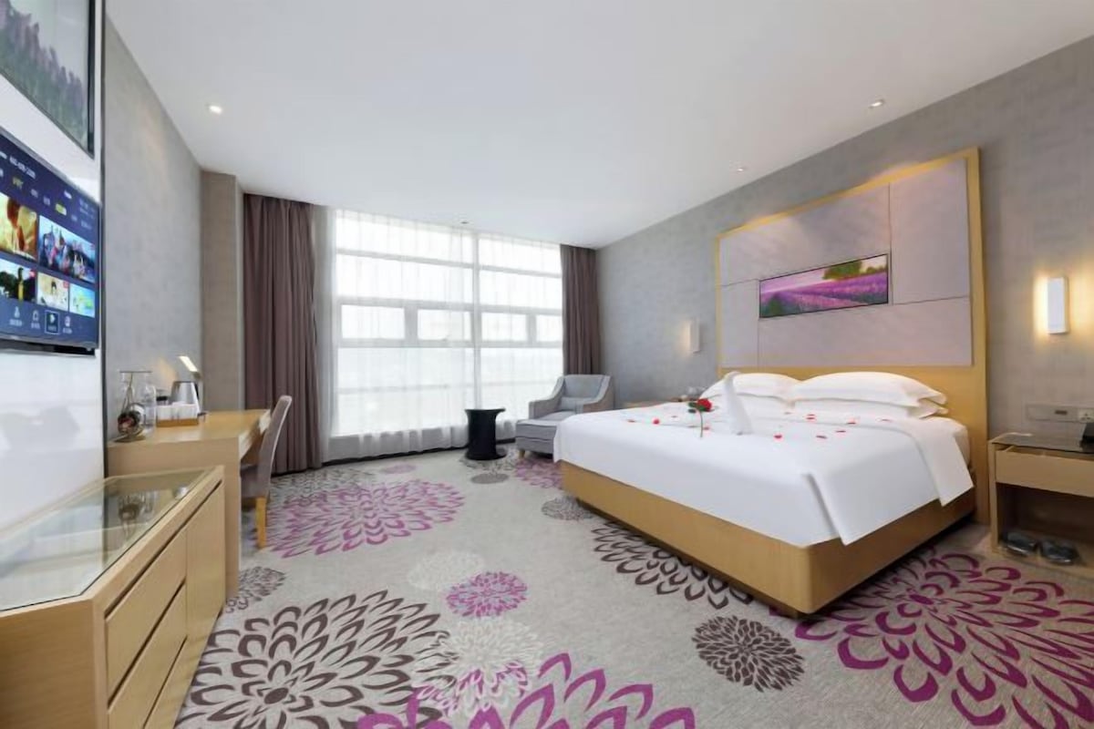 A hotel room with a bed, a desk, a chair, a TV, and a large window.