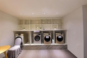 A laundry area with multiple washing machines and a chair. - Lavande Hotel (Dongguan)