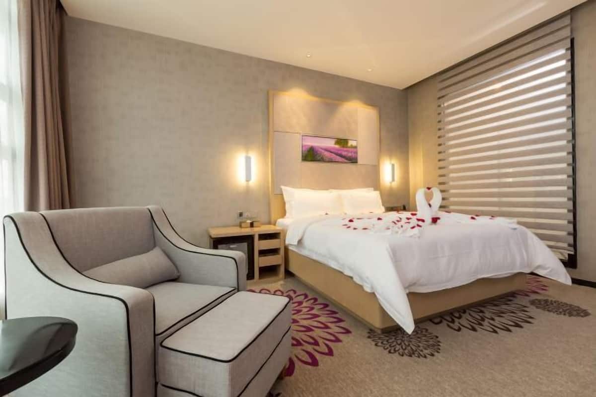 A hotel room with a bed, a sofa, a nightstand, and a wall-mounted picture.