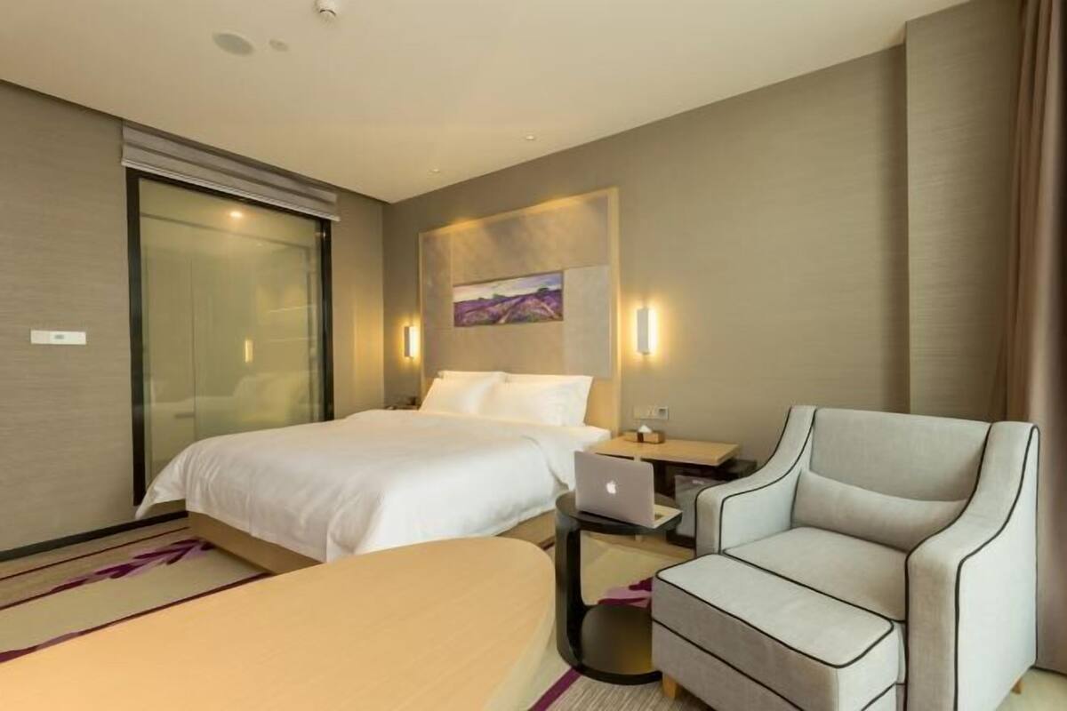 A hotel room with a bed, a desk with a laptop, a chair, and a painting on the wall.