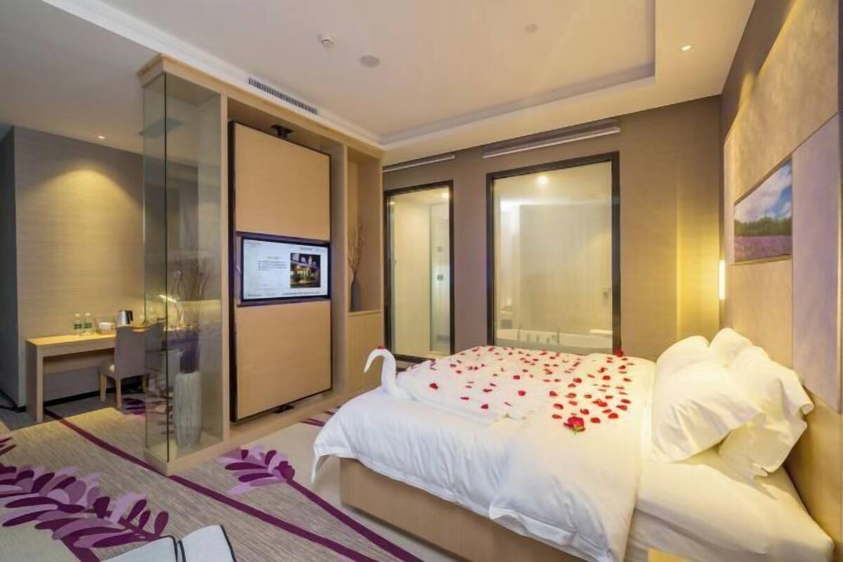 A modern hotel room with a large bed, a desk, and a glass partition.