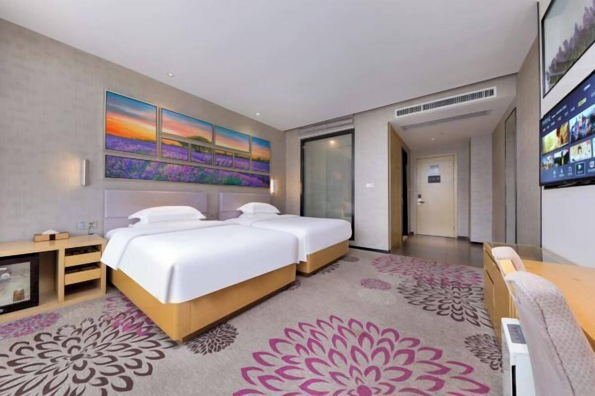 A modern hotel room with a large bed, a TV, a desk, and a wall-mounted artwork.