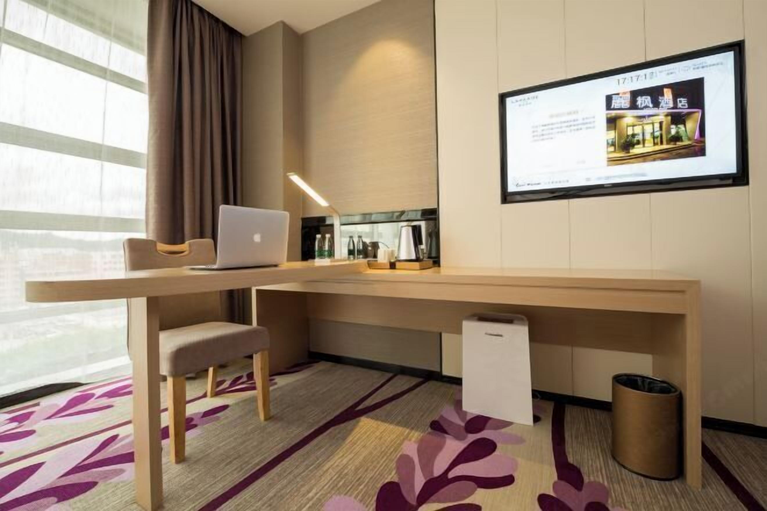 Ein modernes Hotelzimmer mit Schreibtisch, Stuhl, Laptop und Fernseher, der ein Hotelbild zeigt.