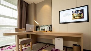 A hotel room with a desk, laptop, chair, and a television mounted on the wall displaying a hotel image. - Lavande Hotel (Dongguan)