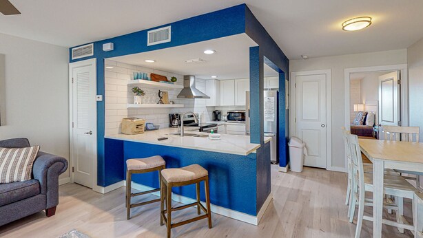 A compact kitchen with a central island, white cabinets, and blue accents. - Ground Floor Condo, Boardwalk to Beach, Shared Pool and Grill (Port Aransas)