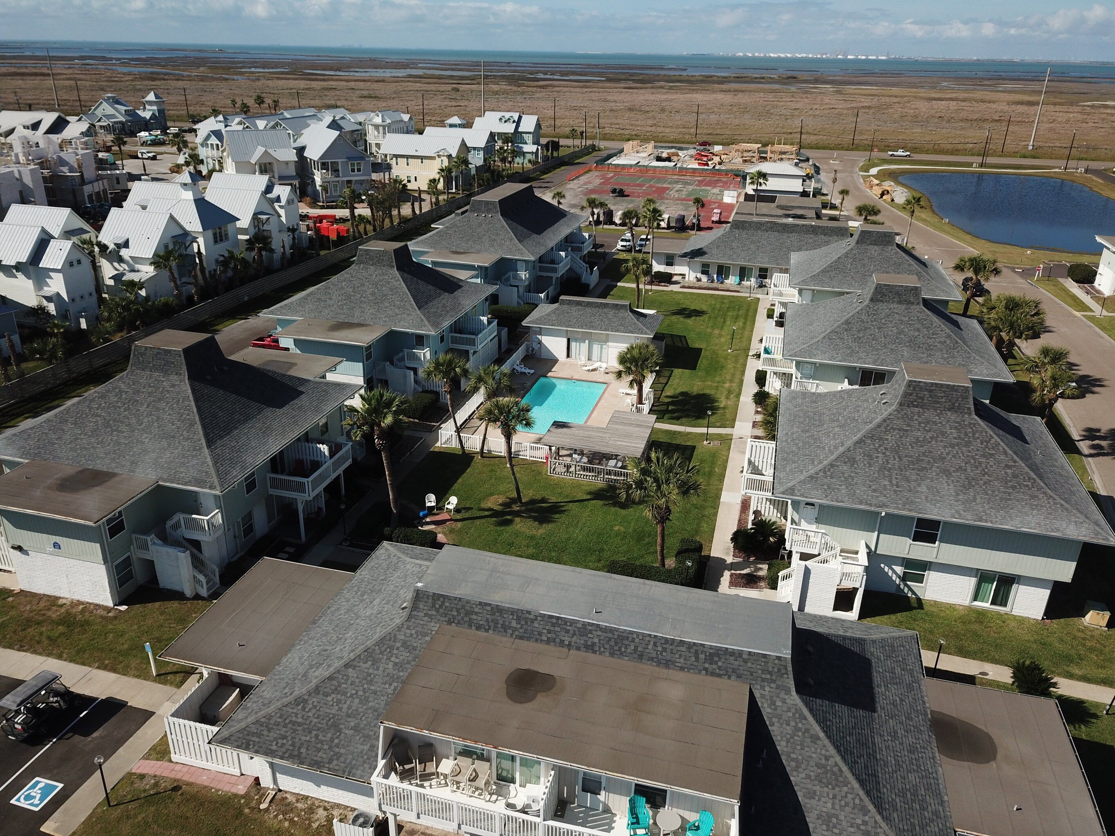 A residential area with houses, a swimming pool, and a large body of water in the background.