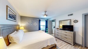 Een slaapkamer met een bed, een dressoir, een televisie en een plafondventilator.
