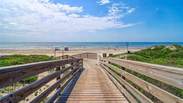 Een houten looppad naar een strand met een heldere lucht en een bord waarop strandnummer 42 staat.