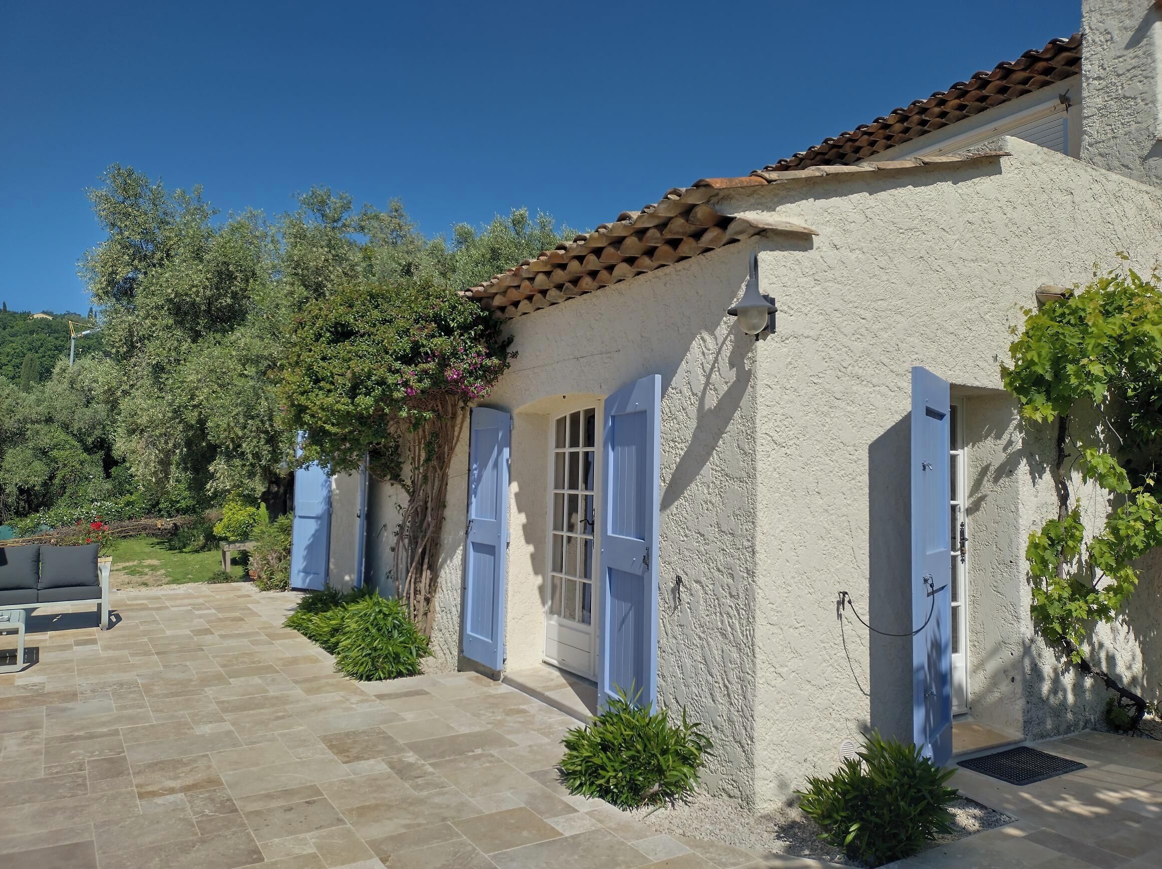 A rustic building with a tiled roof, blue doors, and a stone patio.