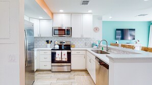 A modern kitchen with white cabinets, stainless steel appliances, and a teal accent wall. - Ground Floor Condo, Shared Pool, Grills and Boardwalk (Port Aransas)