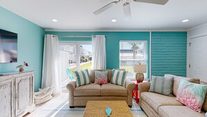 A living room with teal walls, a beige sofa, and a television on a white cabinet. - Ground Floor Condo, Shared Pool, Grills and Boardwalk (Port Aransas)