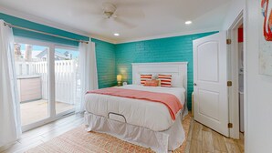 A bedroom with a teal brick wall, white bed, and a sliding glass door to a balcony. - Ground Floor Condo, Shared Pool, Grills and Boardwalk (Port Aransas)