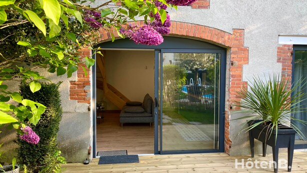 Una casa moderna con puerta de cristal, una terraza de madera y un jardín con flores moradas.