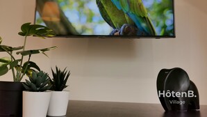 Un televisor mostrando un loro, con plantas en macetas y un objeto negro sobre una mesa.