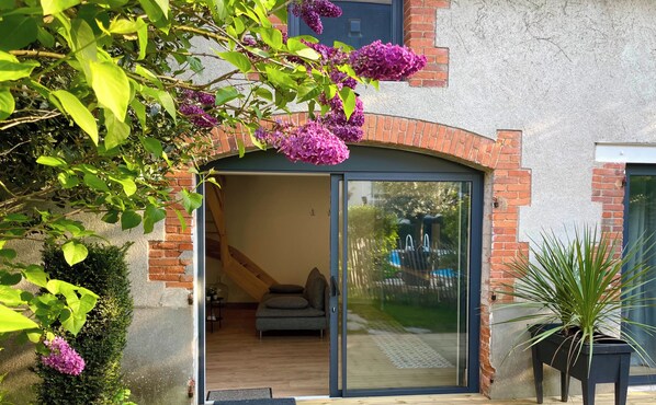 Ein modernes Haus mit Glastür, einer Holterrasse und einem Garten mit violetten Blumen.