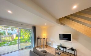 Ein modernes Wohnzimmer mit einem grauen Sofa, einem Fernseher und einem kleinen Tisch mit einer Lampe.
