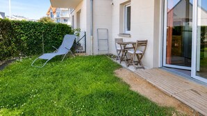 A residential building with a balcony, a small patio with a table and chairs, and a grassy yard. - La Patoune - Garden/50m from the beach/Wifi/Parking (Courseulles-sur-Mer)