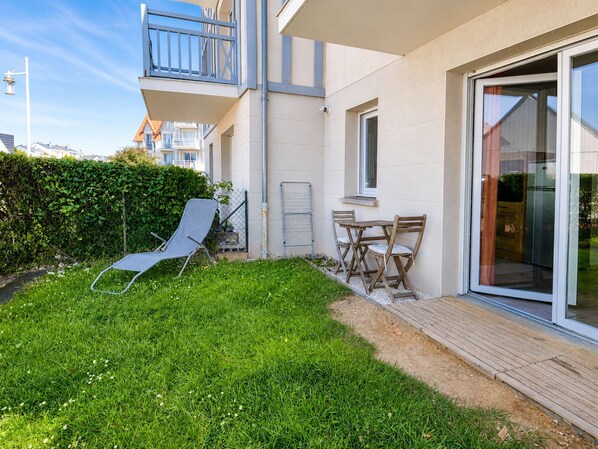 Een woongebouw met een balkon, een klein terras met tafel en stoelen, en een gazon.