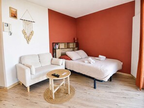 A room with a bed, a sofa, a small table, and a wall-mounted shelf. - La Patoune - Garden/50 m from the beach/Wi-Fi/Parking (Courseulles-sur-Mer)
