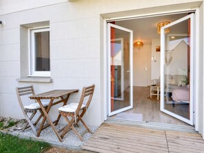 A wooden deck leading to a glass door entrance of a room with a bed, a table, and a chair.