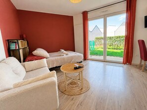 A modern living room with a sofa, a round coffee table, and a bed with a view of the outdoors. - La Patoune - Garden/50 m from the beach/Wi-Fi/Parking (Courseulles-sur-Mer)