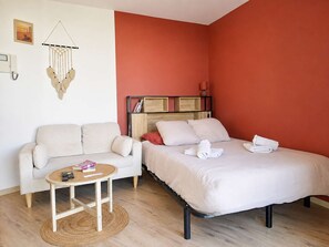 Ein Zimmer mit einem Bett, einem Schlafsofa, einem kleinen Tisch und einem Wandregal.