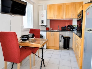 A compact kitchen with a dining area, a washing machine, and a TV mounted on the wall.