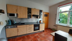 A compact kitchen with wooden cabinets, a built-in oven, and a window with a view of greenery. - Apartment at Levinscherpark, 3km from downtown (Göttingen)