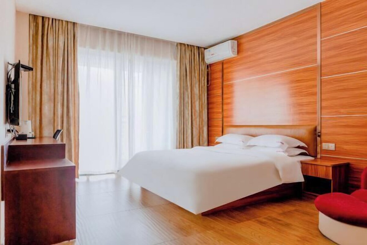 A hotel room with a bed, wooden paneling, a desk, and a red chair.