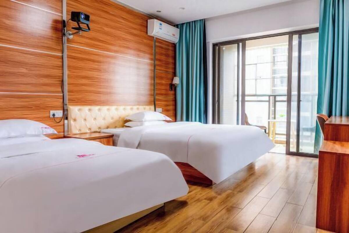 A hotel room with two beds, wooden paneling on the walls, a large window with curtains, and a balcony.