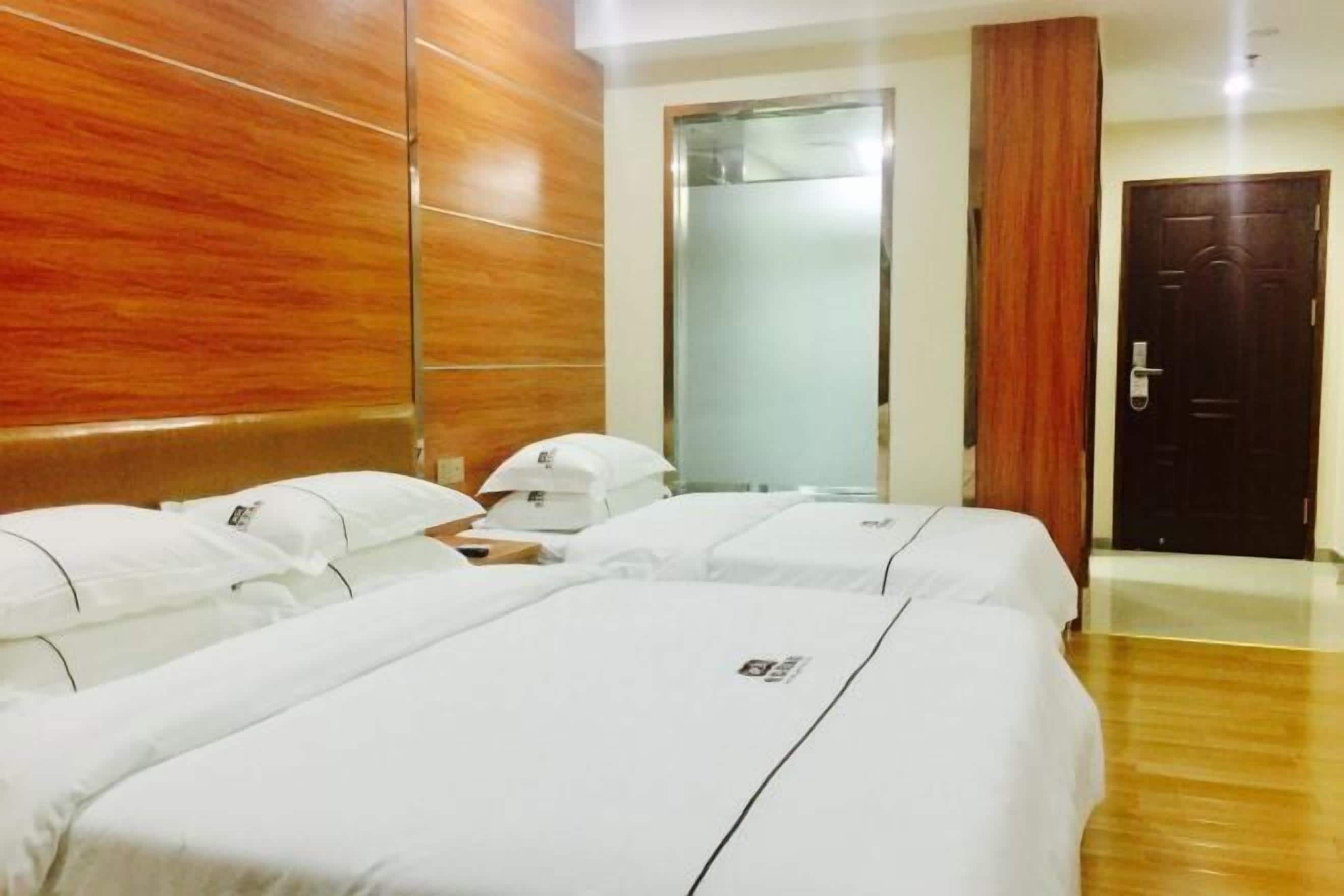 A hotel room with two beds, wooden paneling on the walls, a large mirror, and a door.