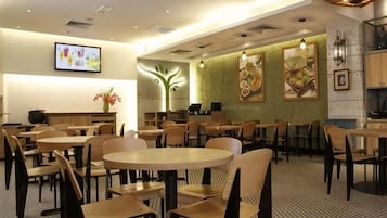 A restaurant with round tables and chairs, a kitchen area, and wall art.