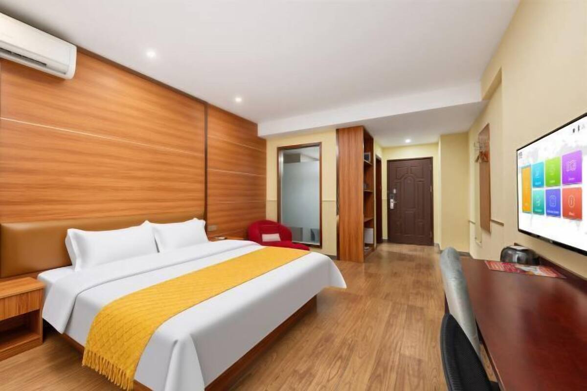 A hotel room with a bed, a TV, a wooden headboard, a red chair, and a door leading to another room.