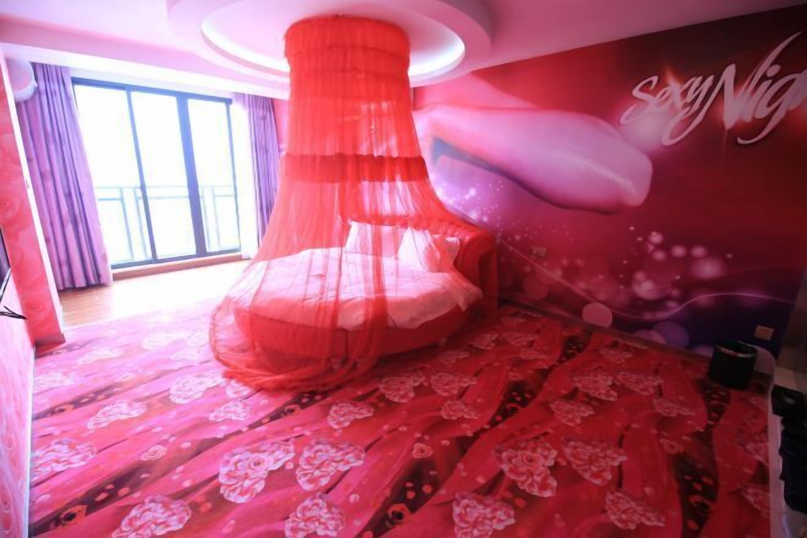 A room with a canopy bed, a large window with curtains, and a wall with a 'Sexy Night' sign.