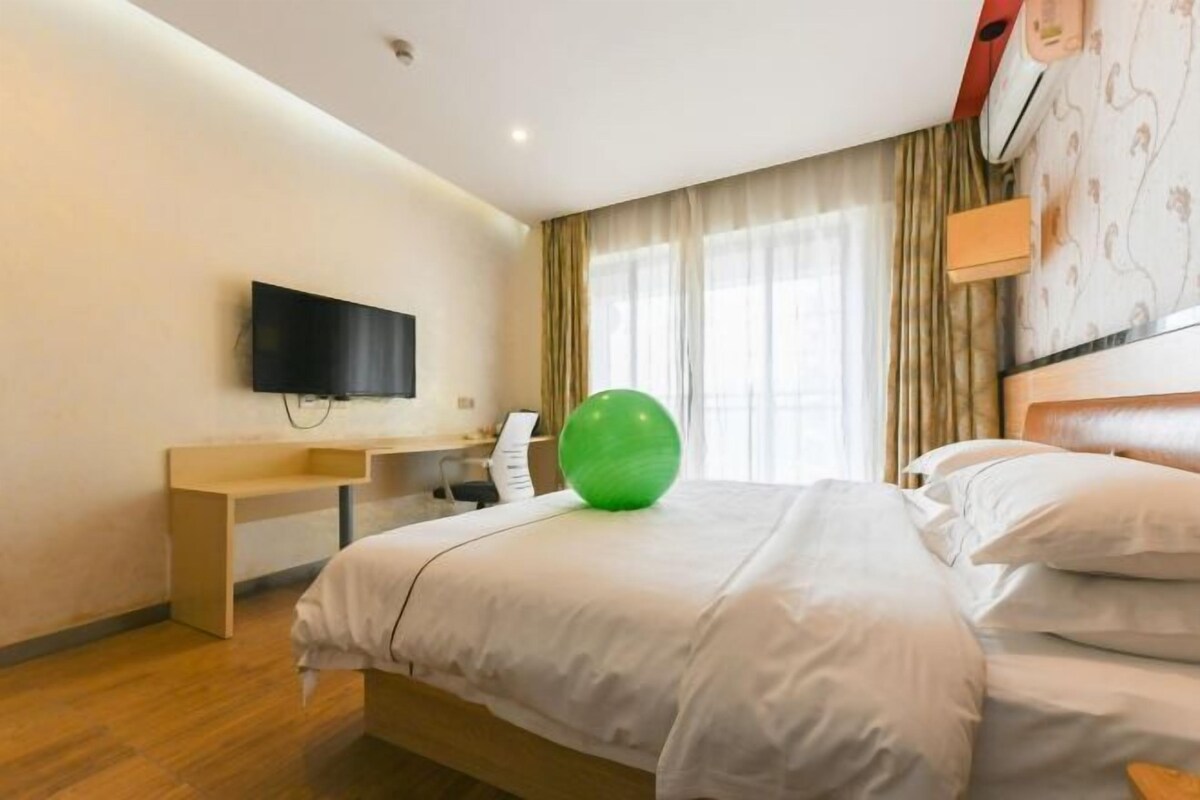 A hotel room with a bed, a desk, a television, and a green exercise ball.